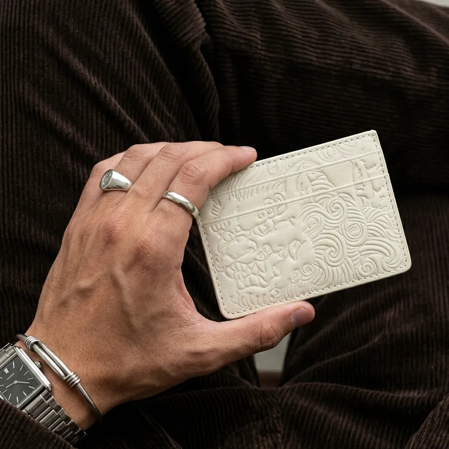 Hand holding a bone white embossed leather card holder against brown corduroy
